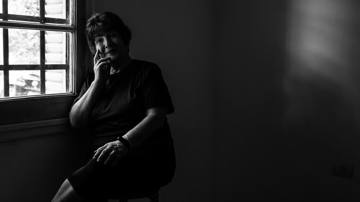 A senior woman sitting thoughtfully by a window in black and white.